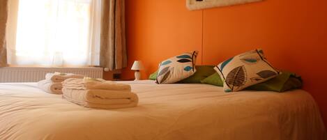 A hotel room with a bed, pillows, a window with curtains, and a wall-mounted penguin artwork.