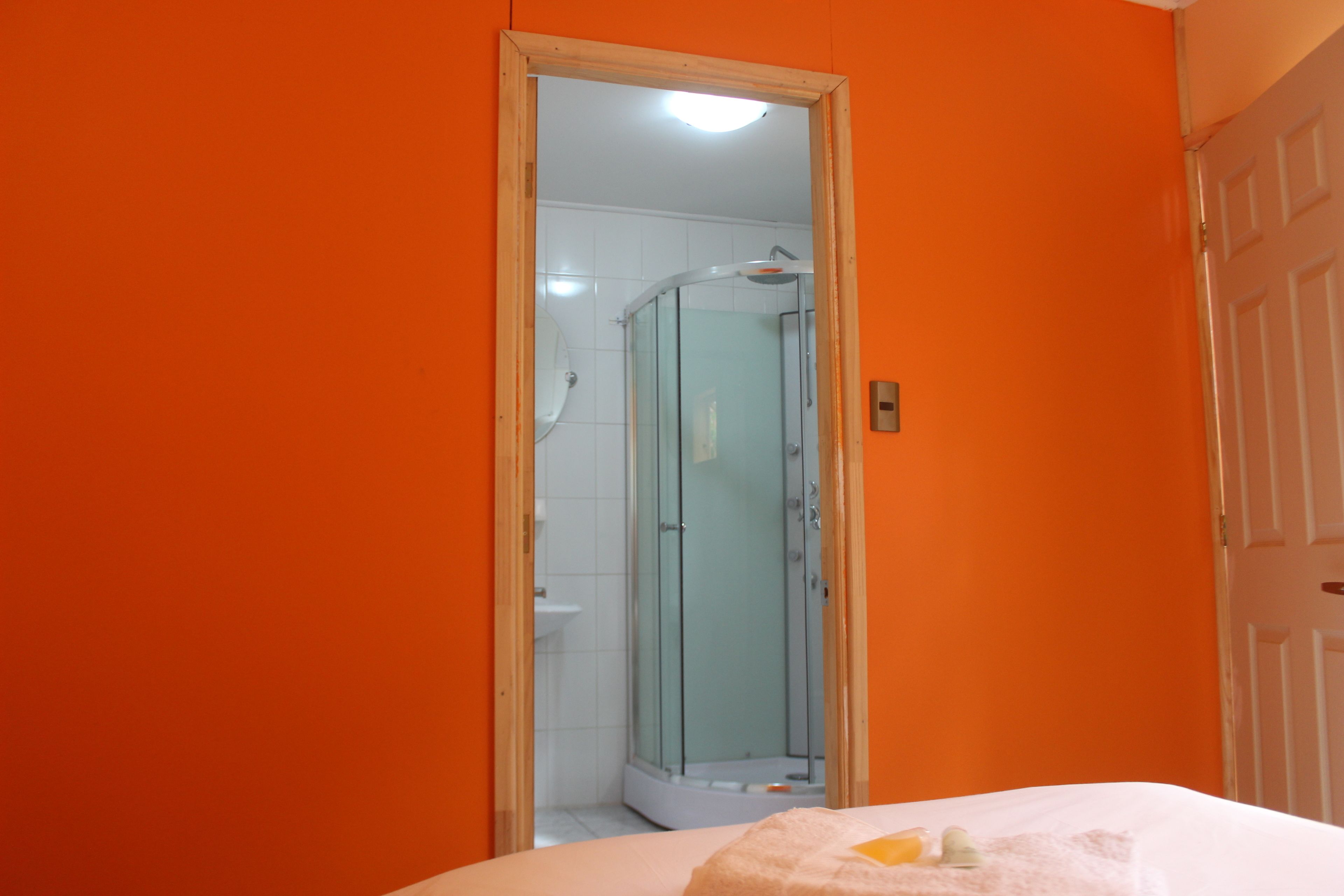 Une salle de bain avec un mur orange, une douche en verre et un lavabo blanc.