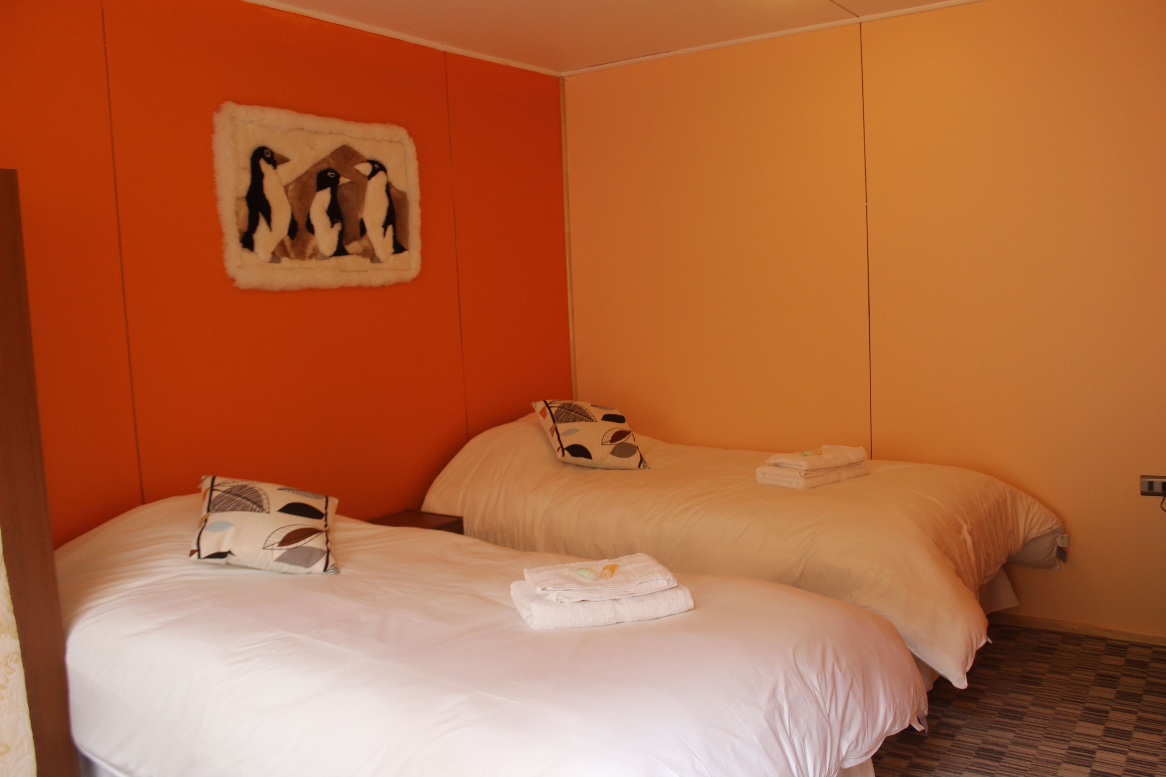 A hotel room with two beds, orange walls, and a decorative penguin wall art.