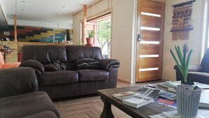 A living room with a brown leather sofa, a coffee table with books and a plant, and a wooden door with a striped pattern.
