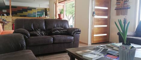 Una sala de estar con un sofá de cuero marrón, una mesa de centro con libros y una planta, y una puerta de madera con un diseño a rayas.
