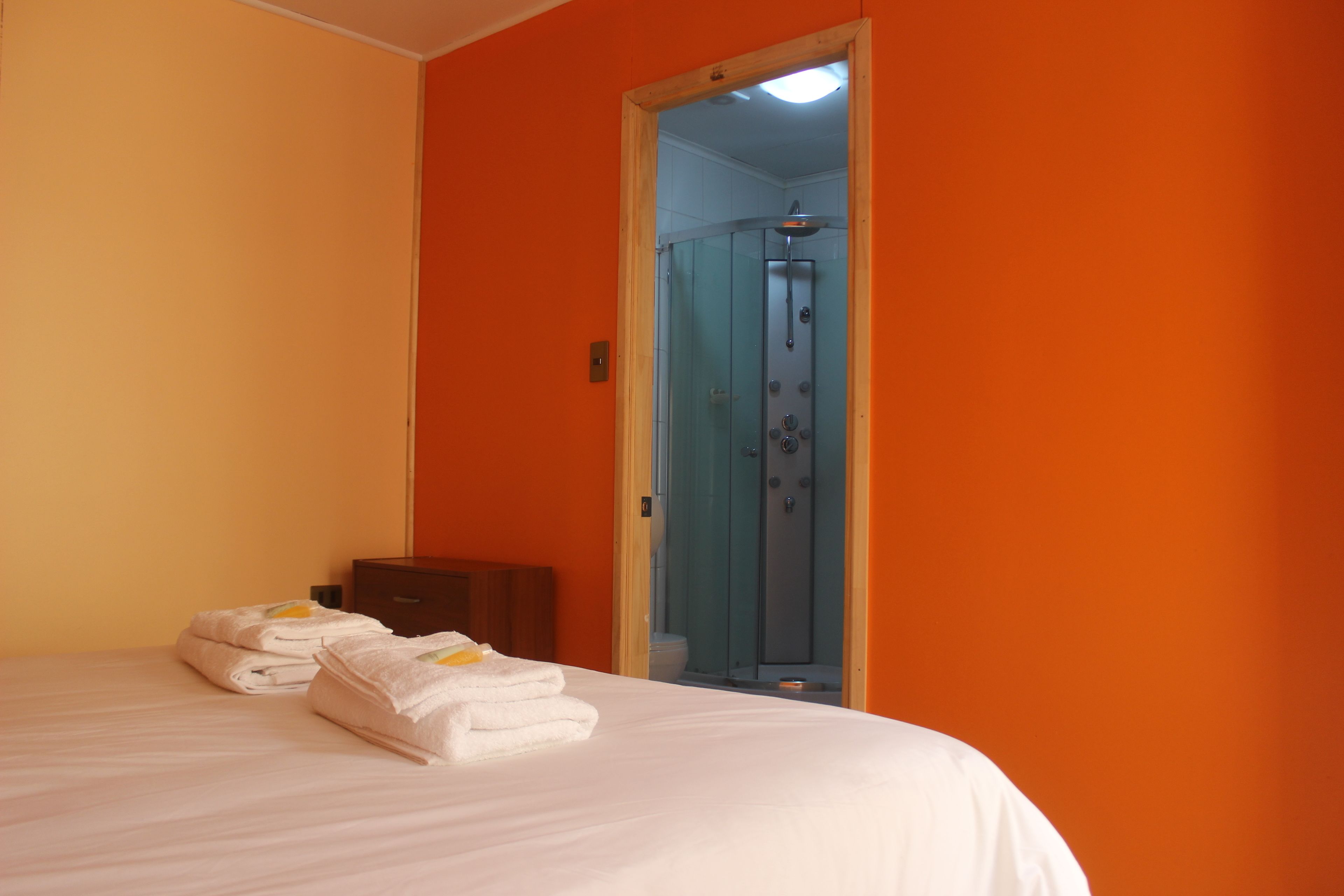 A hotel room with a bed, a wooden nightstand, and a glass shower enclosure.