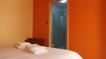 A hotel room with a bed, a wooden nightstand, and a glass shower enclosure.