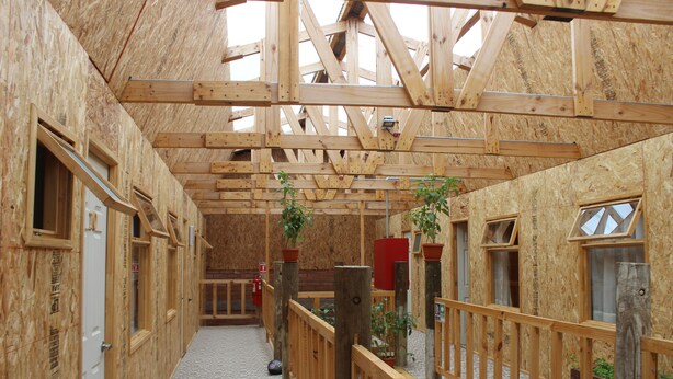 An indoor wooden structure with a high ceiling, wooden railings, and multiple windows.