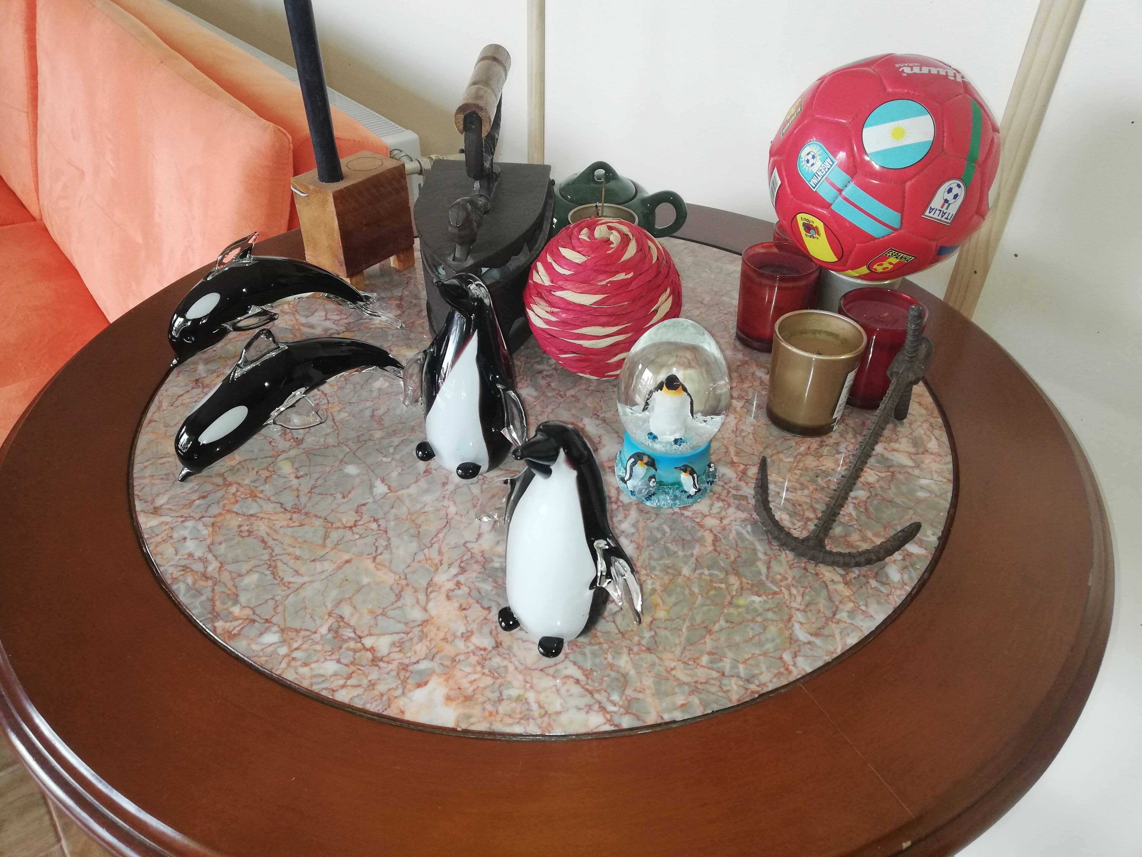Una mesa redonda de madera con tapa de mármol, decorada con una figura de un pingüino, una pelota de fútbol roja, una escultura de vidrio y un gancho.