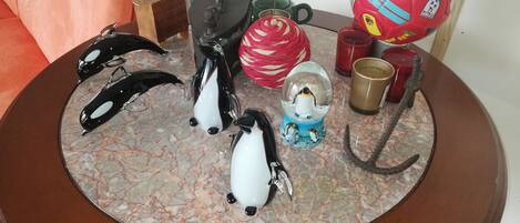 A round wooden table with a marble top, decorated with a penguin figurine, a red soccer ball, a glass sculpture, and a hook.