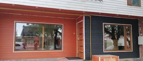 Un edificio con fachada roja, ventanas amplias y un acceso con losetas de piedra.