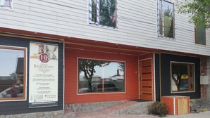 A building with a sign advertising a hotel named 'Hostal Baquedano' in Puerto Natales. It mentions 16 double rooms, a fully equipped private bathroom, Wi-Fi connection, a large dining area, and TV and board games.