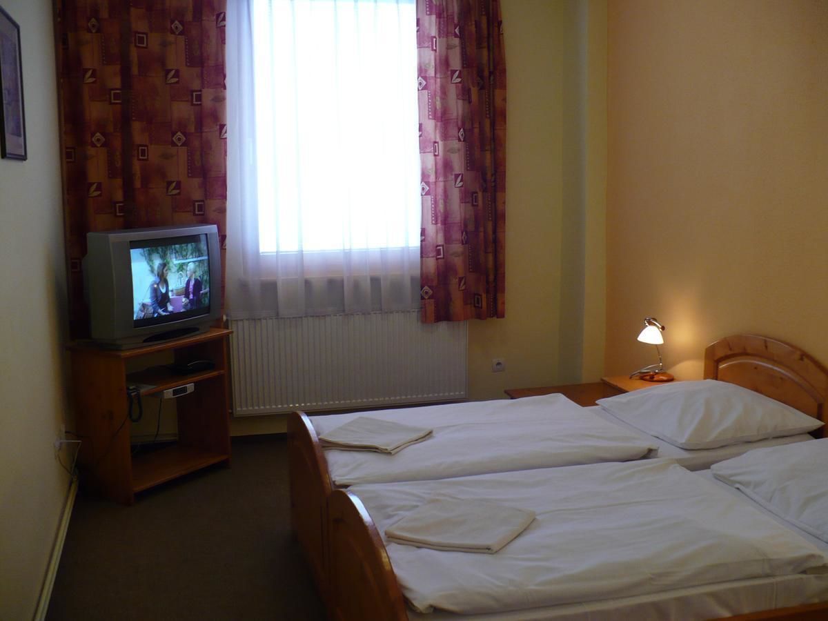 Ein Hotelzimmer mit zwei Betten, einem Fernseher auf einem Holzbalken, einem Fenster mit Vorhängen und einer Nachttischlampe.
