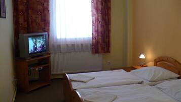 Ein Hotelzimmer mit zwei Betten, einem Fernseher auf einem Holzbalken, einem Fenster mit Vorhängen und einer Nachttischlampe.