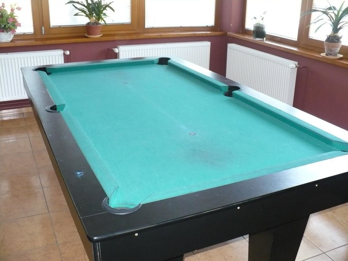 Una mesa de billar en una habitación con suelo de baldosas y una ventana con persianas.