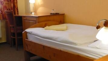 Una cama individual con cabecera de madera, una mesita de noche con lámpara, un escritorio y una silla en una habitación de hotel.