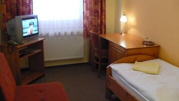A hotel room with a bed, a desk, a chair, a television, and a lamp.