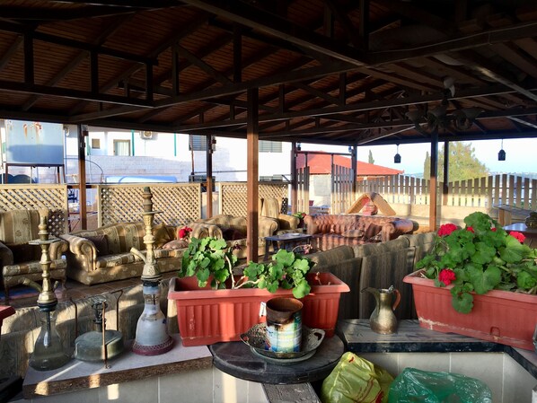 Un espacio de estar al aire libre cubierto con muebles de madera, plantas en macetas y lámparas tradicionales.