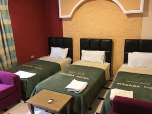 Habitación de hotel con dos camas, cada una con cubrecama verde y un almohadón, y una pequeña mesa de madera con un teléfono encima.