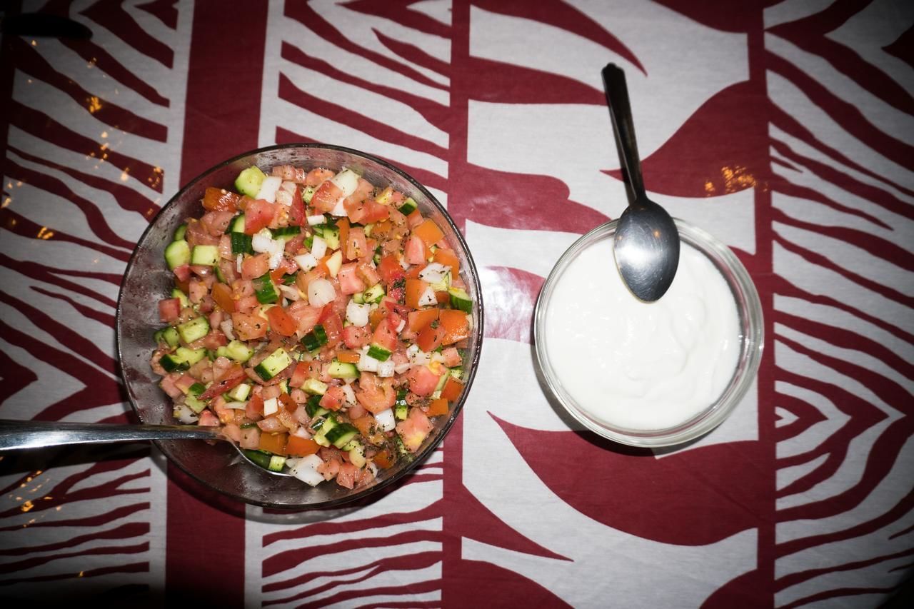 A bowl of chopped vegetables and a spoon, placed on a patterned tablecloth.