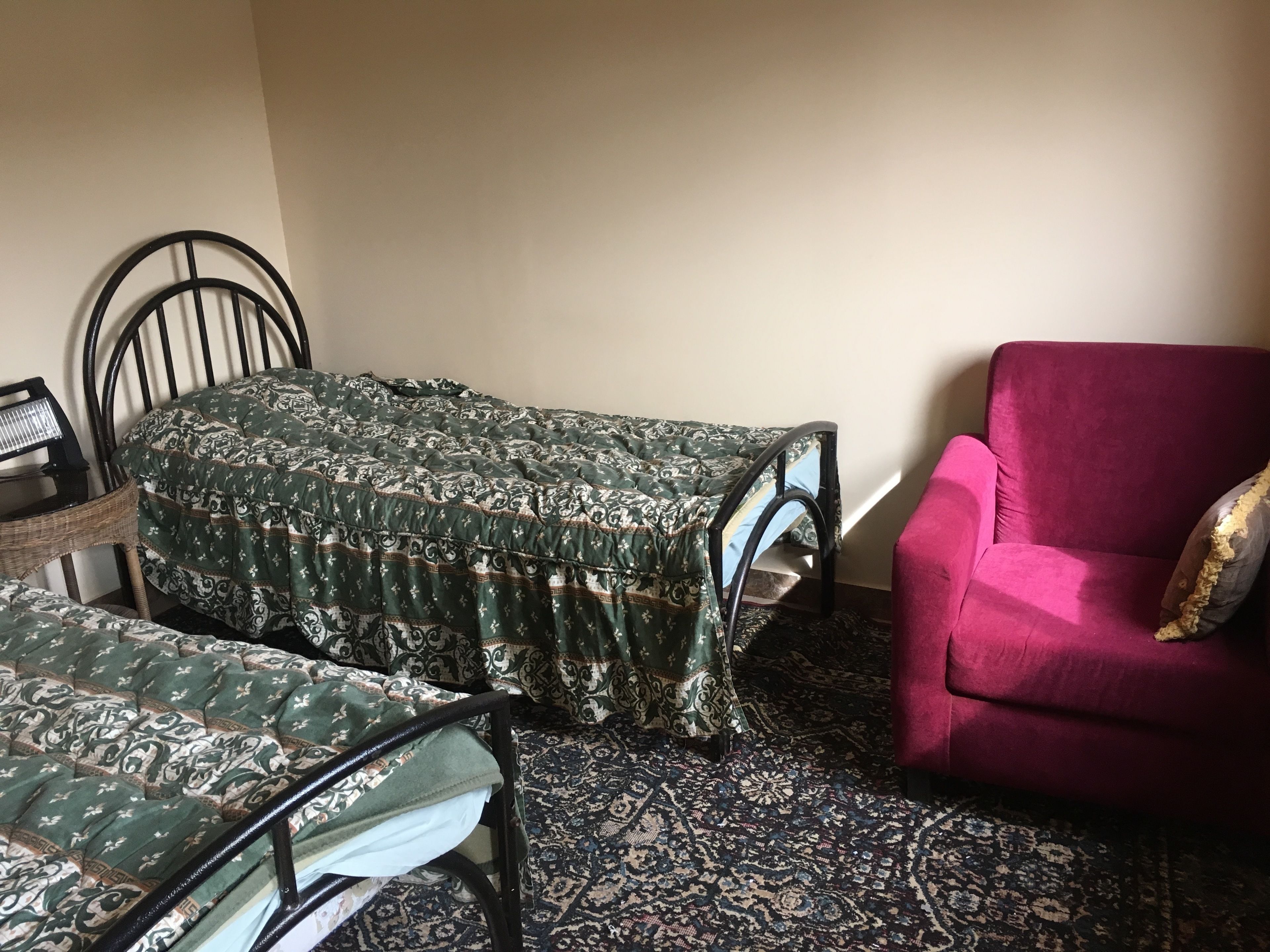 Una habitación con dos camas individuales, un sillón rojo y una alfombra estampada.