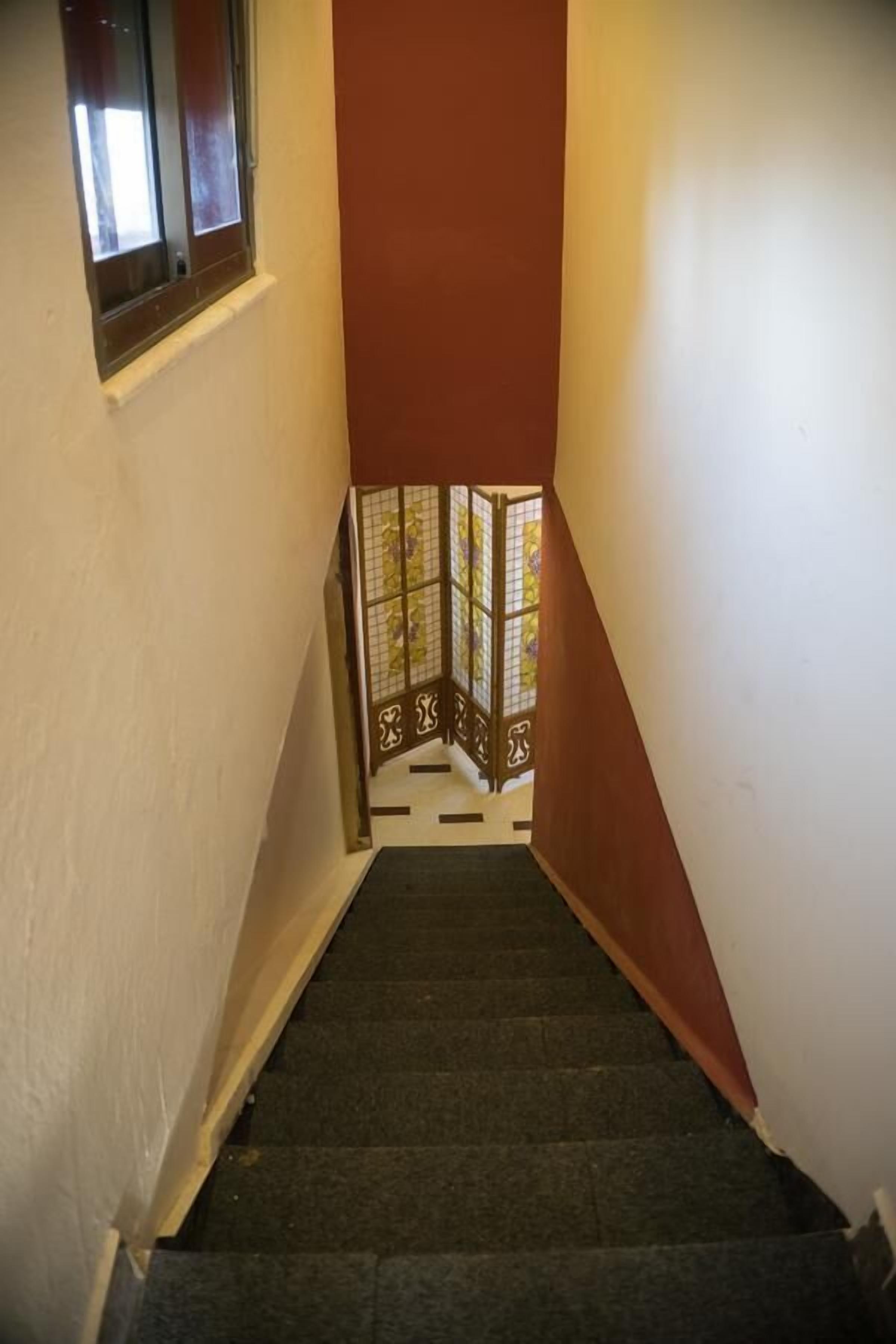 A narrow stairway with a red wall and a window at the top.