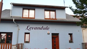 A building with the name "Levandule" on its facade, featuring a red door, multiple windows, and wooden flower planters. - Penzion Levandule (Brno)