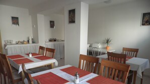A dining area with multiple tables and chairs, a kitchen area in the background, and a potted plant on a small table. - Penzion Levandule (Brno)