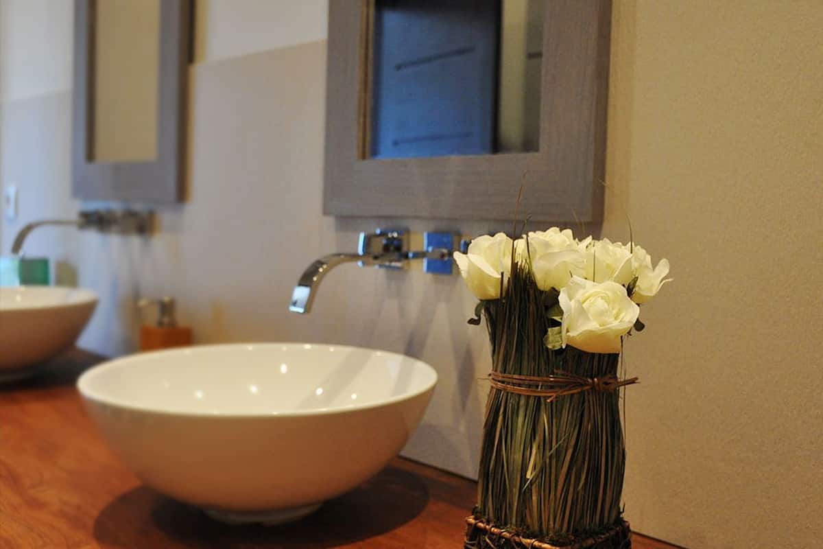 A bathroom with a white sink, a mirror, and a vase with white flowers.