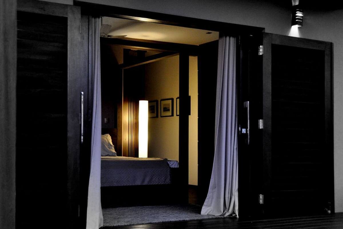 A bedroom with a bed, a nightstand, a lamp, and a door leading to another room.