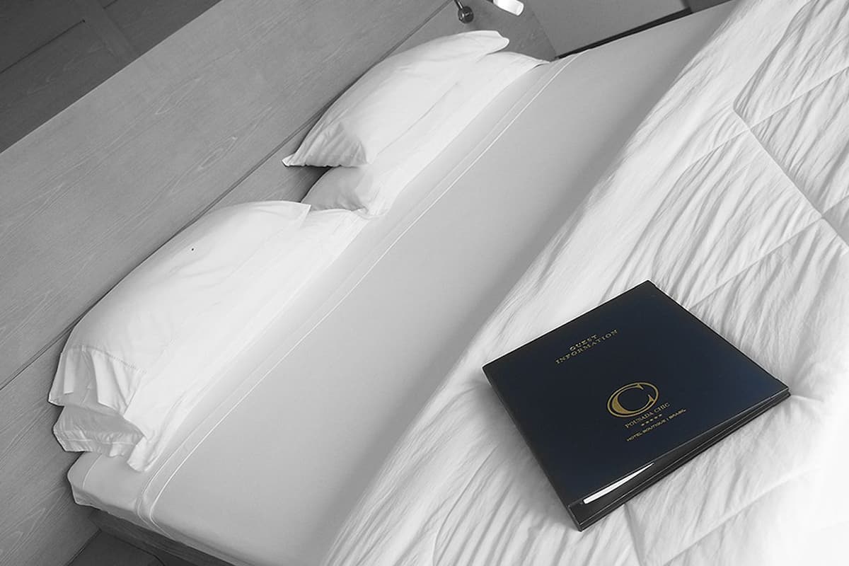 A neatly made bed with white linens and a black box with gold text on a wooden floor.