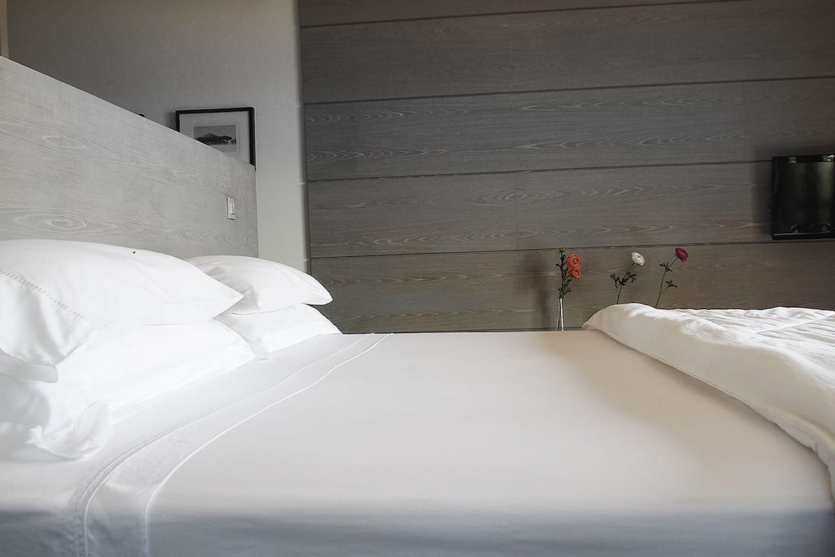 A neatly made bed with white linens, a wooden headboard, and a small vase with flowers on the nightstand.
