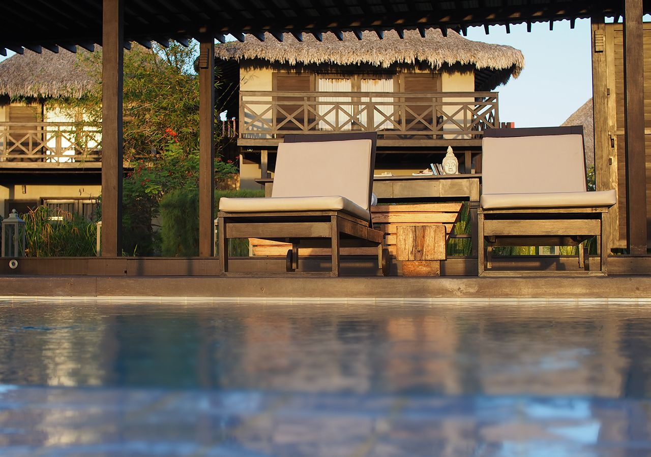 A poolside area with wooden lounge chairs and a thatched-roof structure.