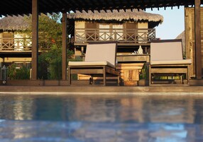 A poolside area with wooden lounge chairs and a thatched-roof structure.