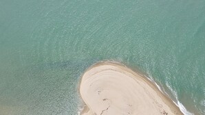 Vista aérea de uma praia com extensa faixa de areia e águas calmas.