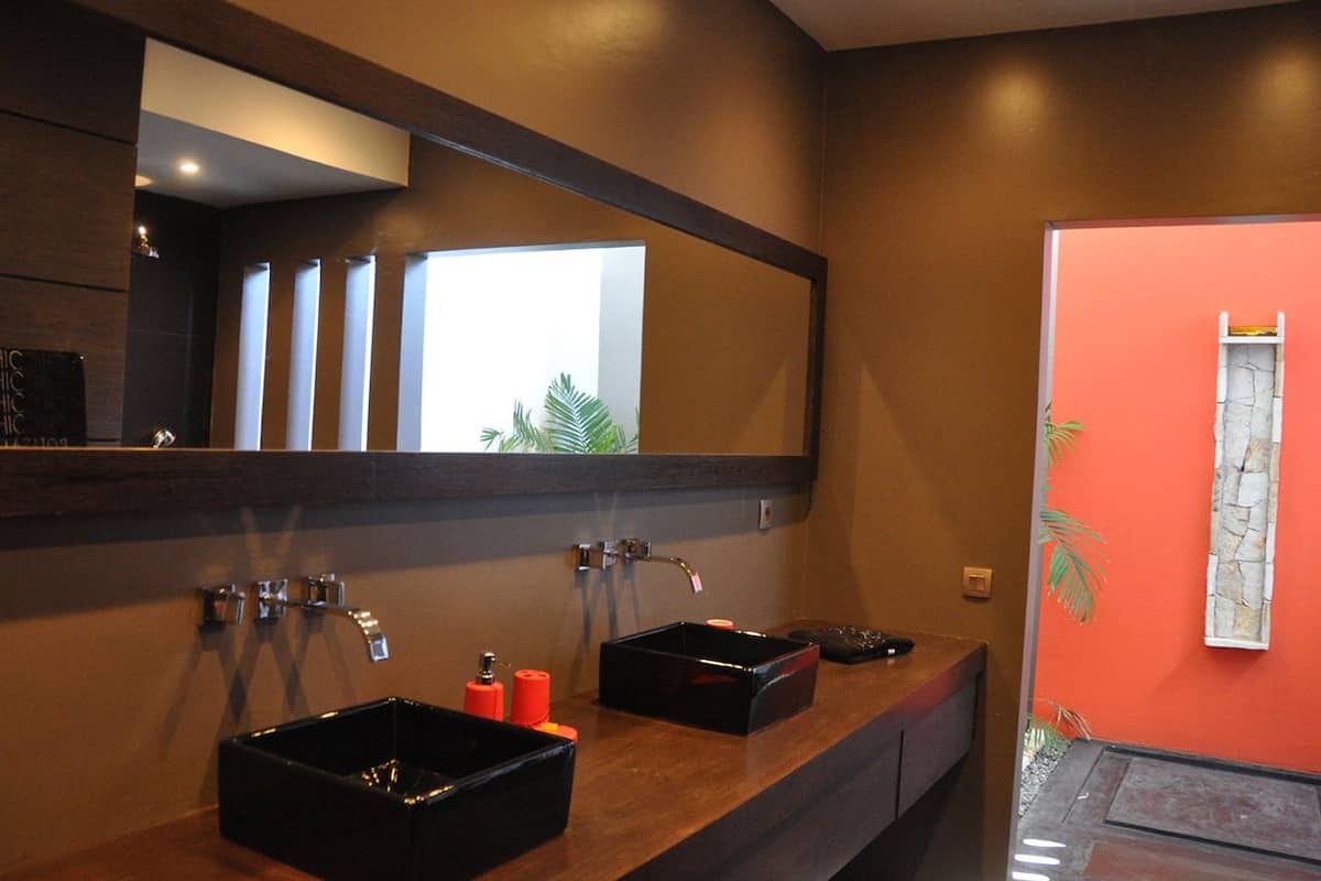 A bathroom with two black sinks, a large mirror, and a red accent wall.
