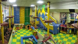 Un área de juegos interior con diversas estructuras para escalar, toboganes y un piso a cuadros.