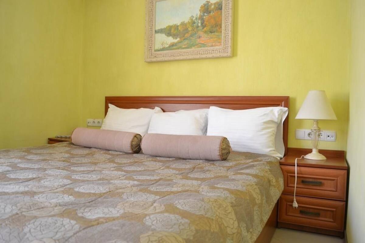 A neatly made bed with a patterned bedspread, a wooden headboard, and a bedside lamp.