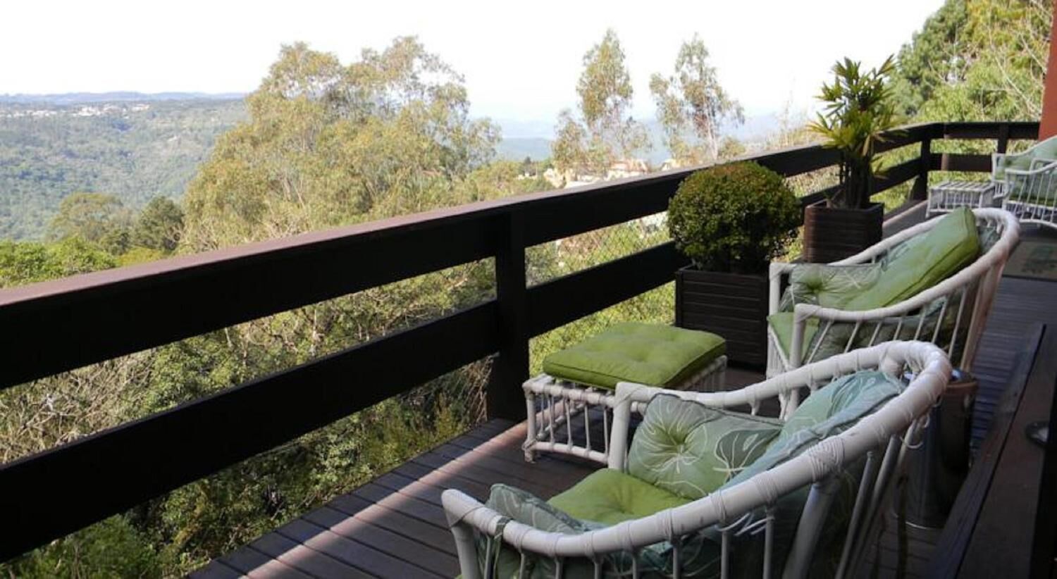 Une terrasse dotée de chaises et de coussins en osier, offrant une vue sur un paysage boisé.