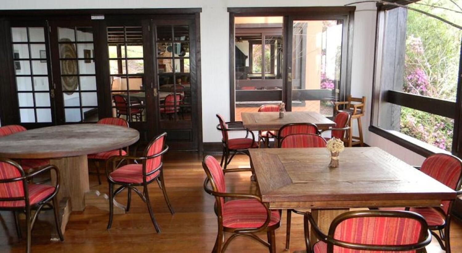 A dining area with a wooden table and red upholstered chairs, large windows with a view of greenery, and traditional sliding doors.