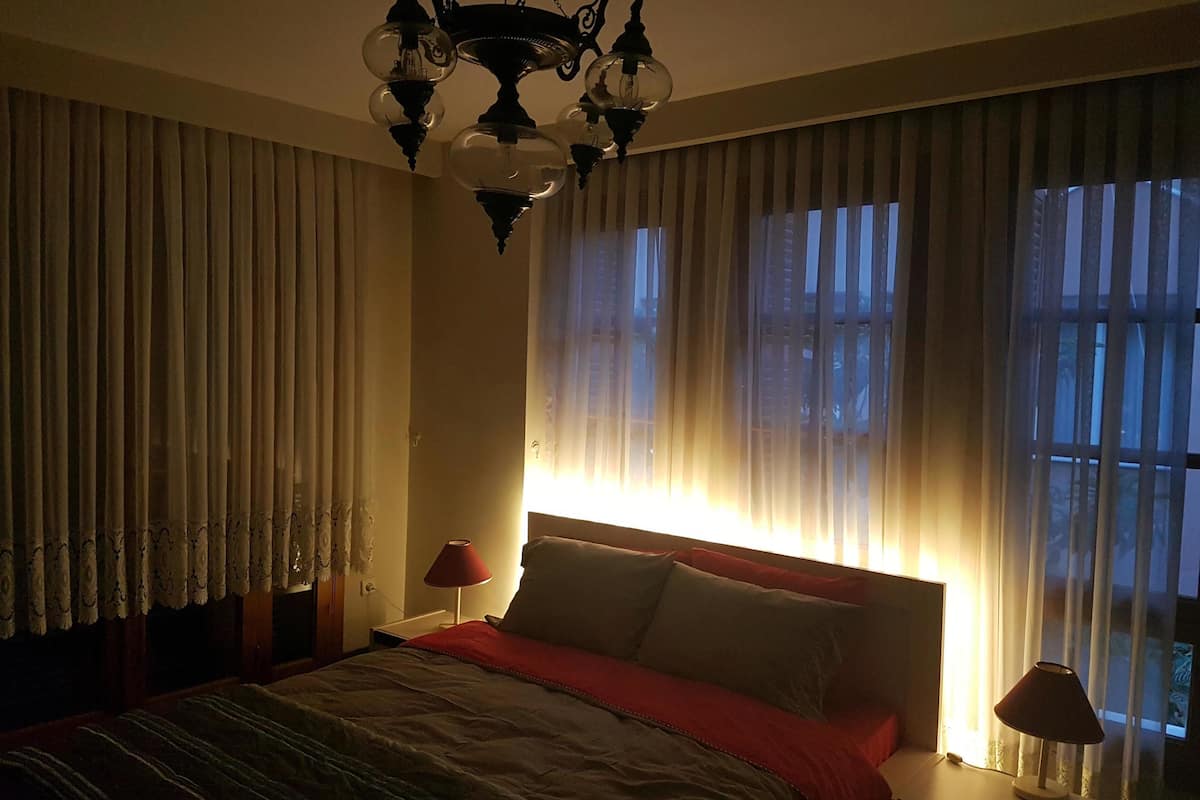 Une chambre à coucher avec un lit, une table de chevet, une lampe, un lustre et des rideaux.
