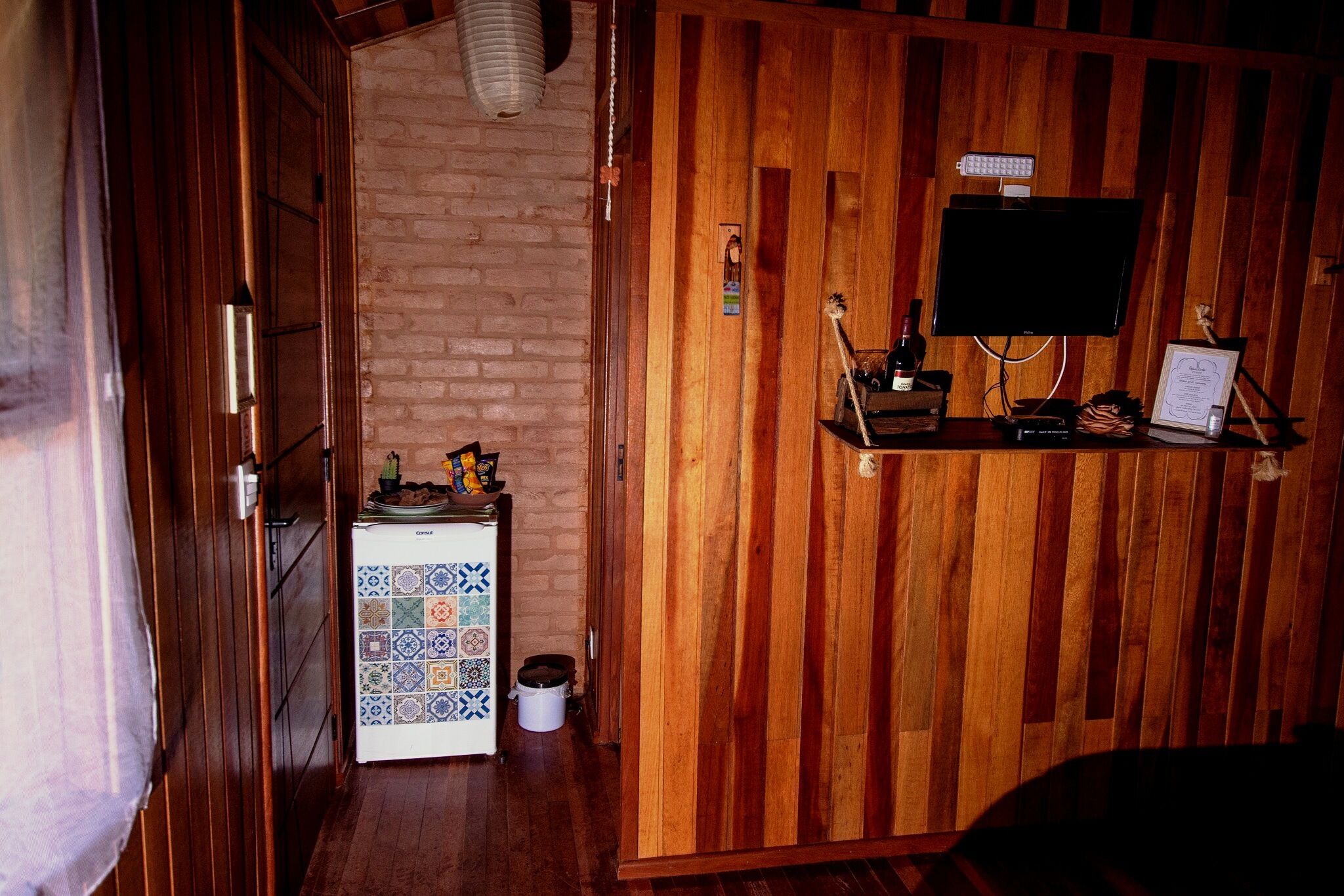 A room with a wooden panel wall, a television mounted on a wooden shelf, a small table with a decorative item, and a tiled cabinet.