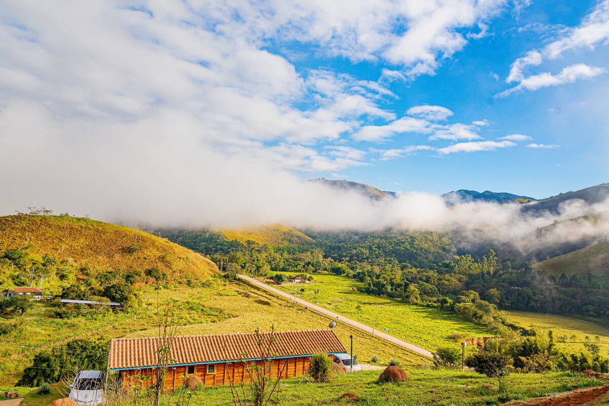 A rural landscape with a house on a hill, surrounded by greenery and mountains.