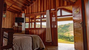 Un dormitorio de cabaña de madera con una cama, un televisor y un ventanal con vistas al exterior.