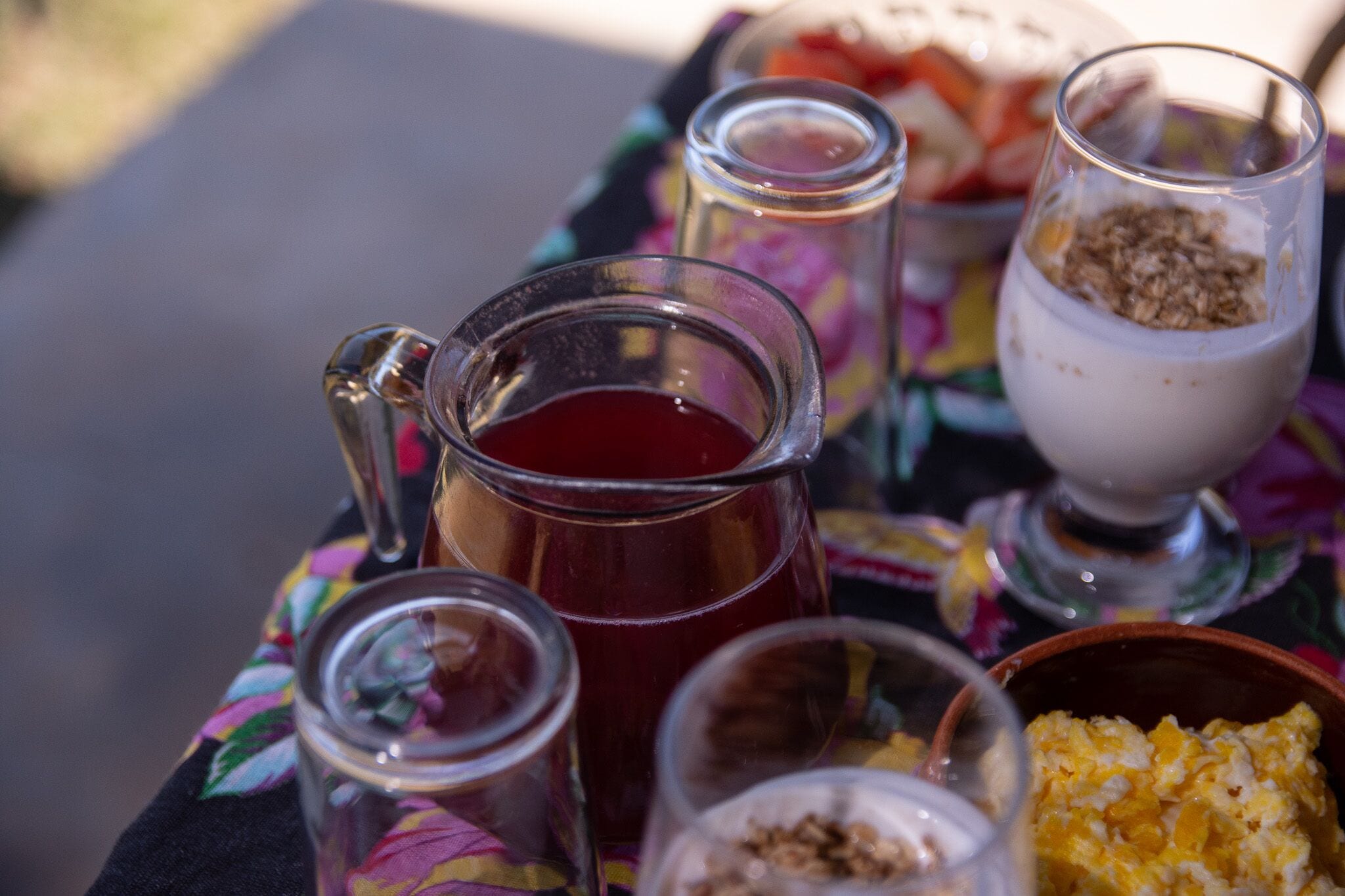 Una mesa con una jofaina de bebida roja, un vaso de yogur con granola y un bol de fruta.