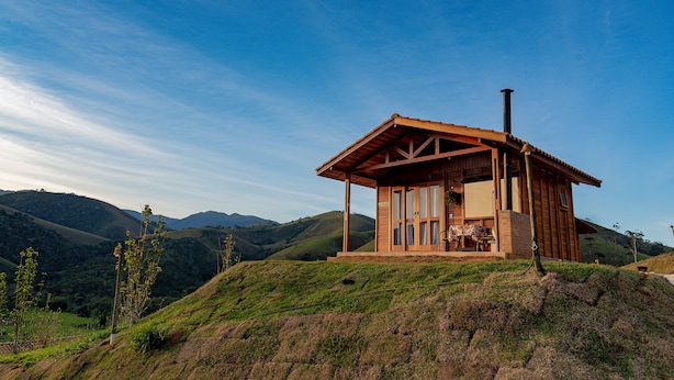 Una cabaña de madera con balcón, situada en una colina cubierta de hierba y vistas a ondulantes colinas al fondo.