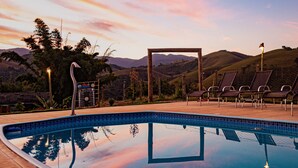 Una piscina con vistas a colinas, un quiosco y sillas de descanso.