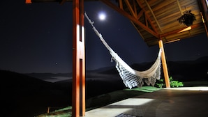 Una hamaca bajo una estructura de madera, con un cielo nocturno y una luna de fondo.