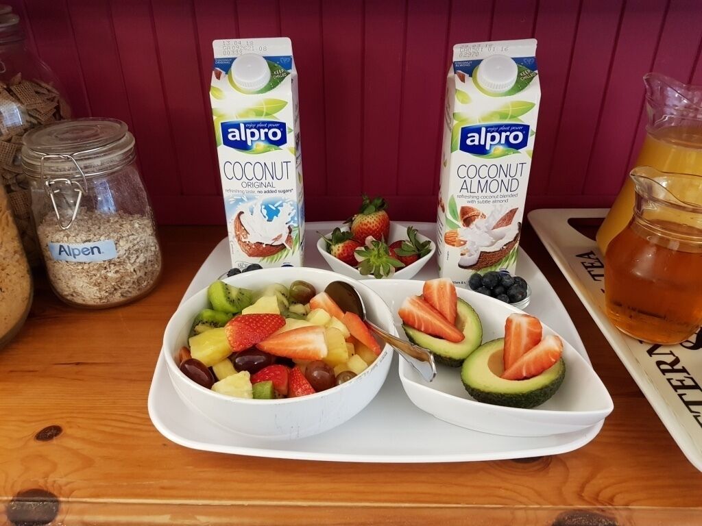 Een ontbijfwagen met fruit, twee pakken Alpro cocos-amand melk, een pot Alpen havermout en een karaf sap.