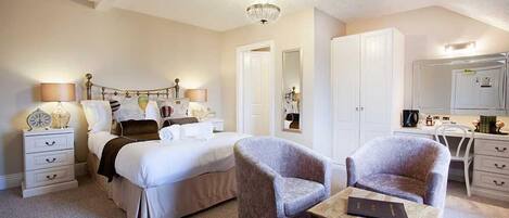 Un dormitorio con cama, dos sillones, una mesa de madera, cómoda, espejo y candelabro.
