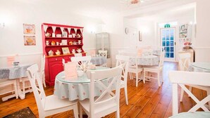 A cozy dining area with white chairs and tables, a red display cabinet with tea sets, and a chandelier. - Number 61 Guest House and Tea Room (North Shields)
