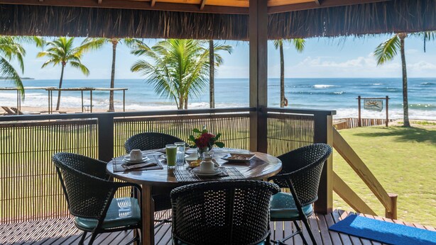 Un espacio de comedor al aire libre con techo y vistas al océano y palmeras.