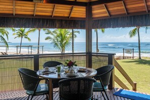 A covered outdoor dining area with a view of the ocean and palm trees. - Pousada Lagoa do Cassange (Maraú)