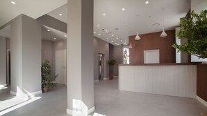 A spacious lobby with a reception desk, potted plants, and a large window allowing natural light.